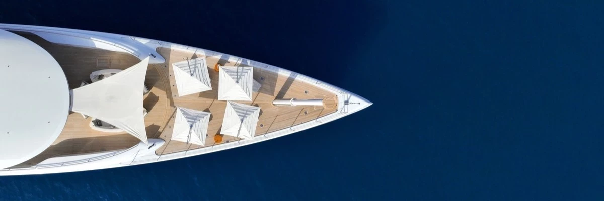 Vista aerea della prua di un superyacht con ponte in teak, prendisole e vele ombreggianti — noleggio di yacht di lusso con equipaggio