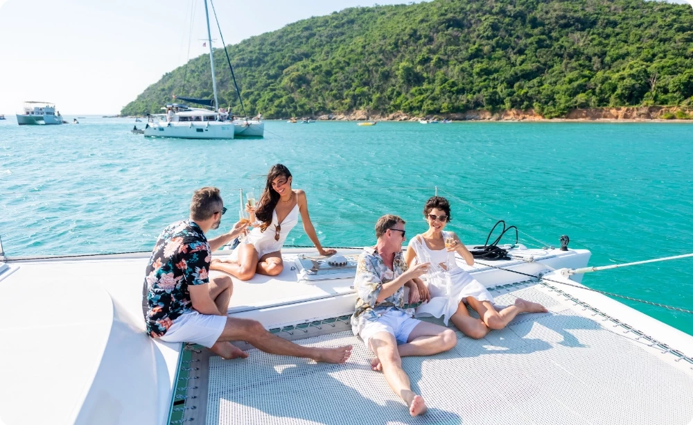 Quattro amici rilassati sul trampolino di un catamarano all'ancora in una baia turchese