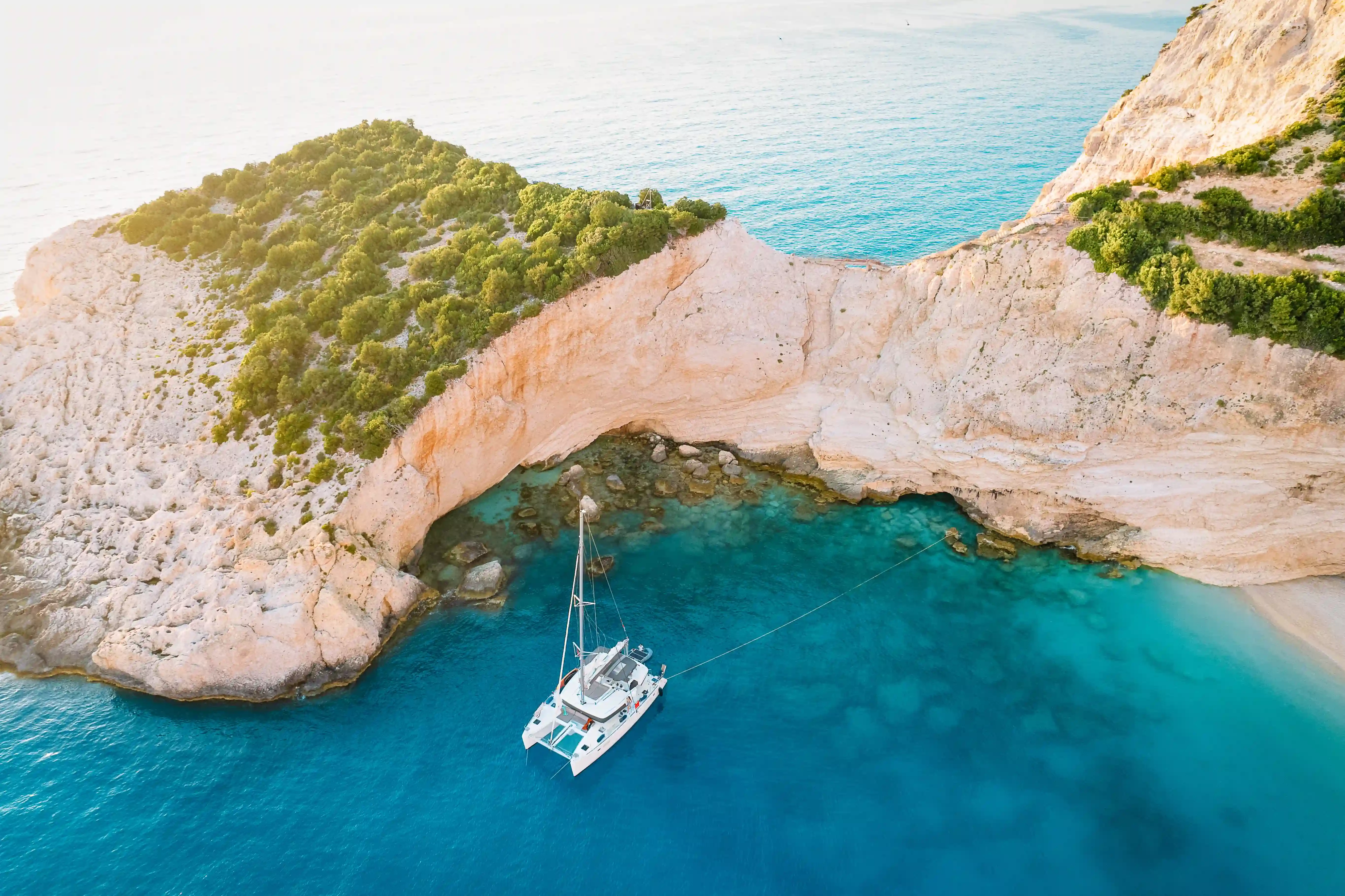 Voilier au mouillage dans une crique grecque aux eaux turquoise. Catamaran au mouillage dans une crique aux eaux cristallines bord&eacute;e de falaises calcaires, vu depuis les airs.