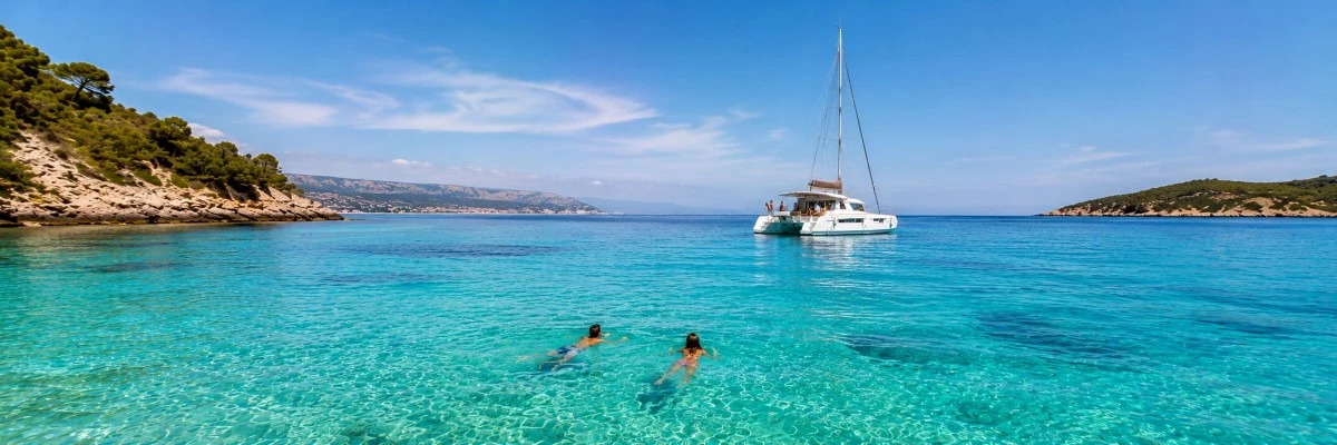 Baignade dans une eau turquoise cristalline devant un catamaran ancré dans une crique abritée, idéale pour une croisière en famille