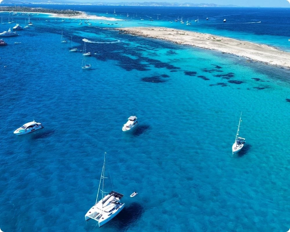 Vue aérienne d'un mouillage à Formentera aux Baléares, catamaran, voiliers et yachts ancrés sur des eaux turquoise transparentes face à la plage de sable blanc de Ses Illetes