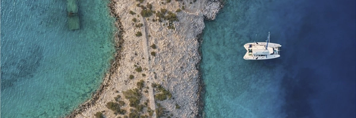 vue aérienne d'un catamaran au mouillage près d'une pointe rocheuse aux eaux turquoise en Corse du Sud