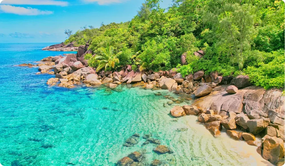 Vue aérienne d'Anse Major, à Mahé, montrant une crique bordée de rochers de granit, une végétation tropicale luxuriante et une eau turquoise cristalline aux Seychelles.