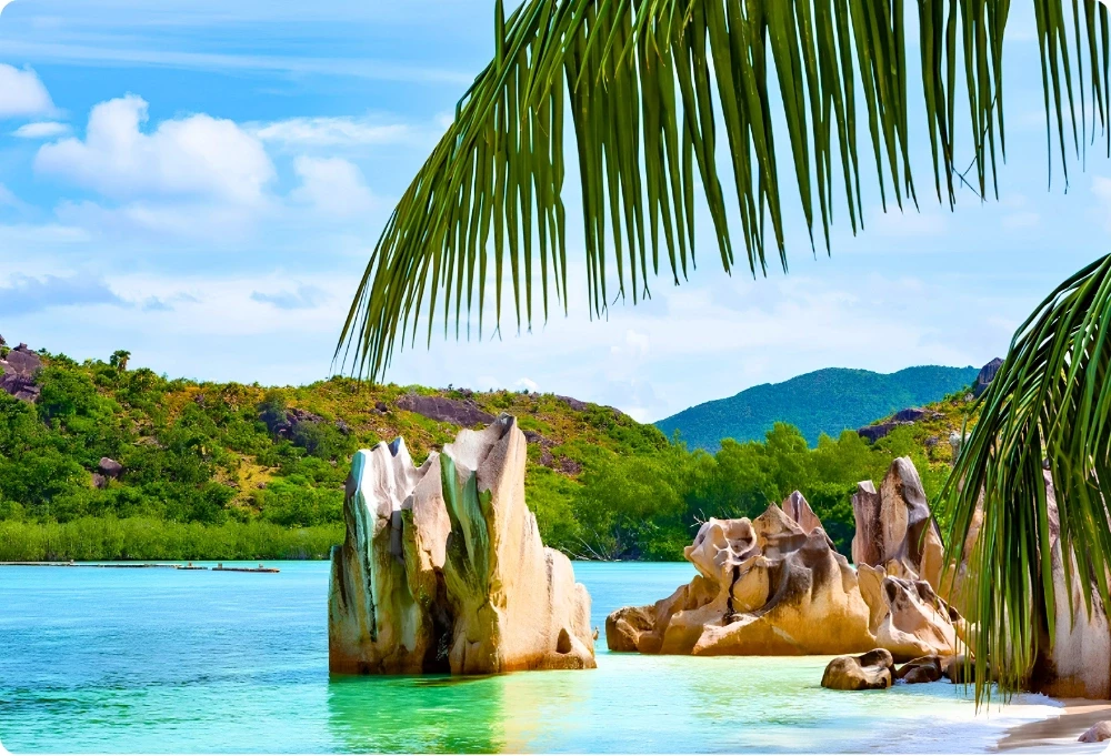Rochers de granit émergeant d'un lagon turquoise sur l'île de Curieuse, aux Seychelles, avec une végétation tropicale en arrière-plan.