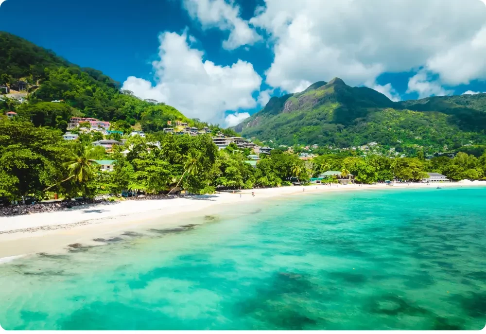 Vue de la plage de Beau Vallon aux Seychelles avec son eau turquoise cristalline, son sable blanc, ses montagnes verdoyantes et sa végétation tropicale, sur l'île de Mahé.