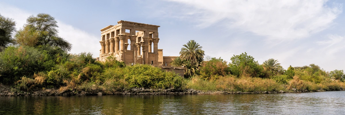 Philae Temple on the banks of the Nile, surrounded by lush vegetation, as seen from a dahabiya during a cruise in Egypt.