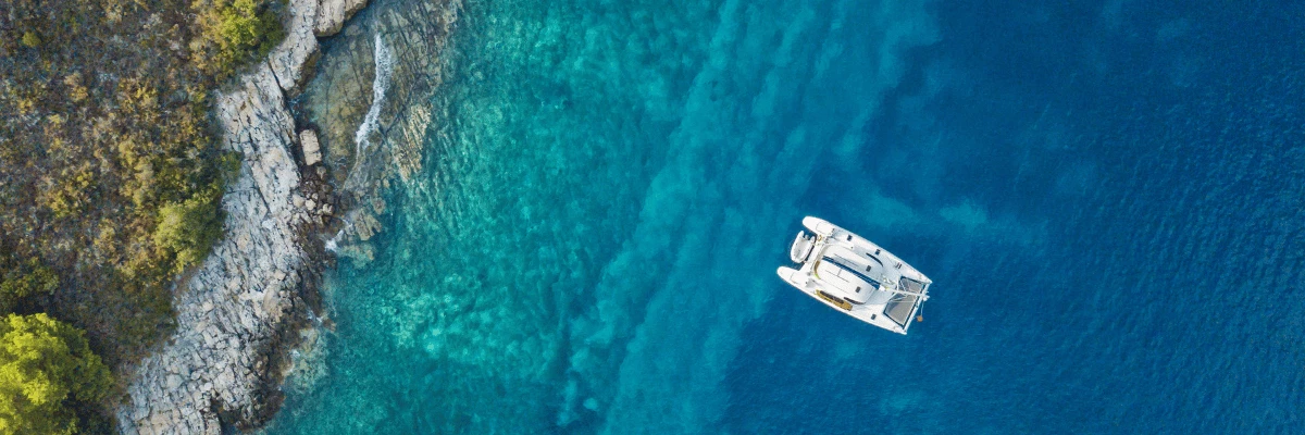 vue panoramique d'un catamaran s'éloignant de la côte sur une mer avec un nuancier de bleus