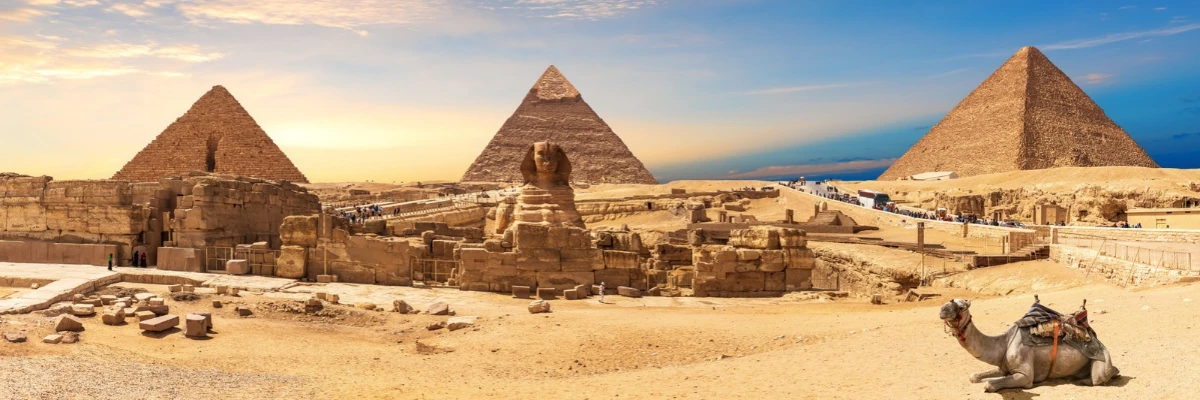 Panoramic view of the Giza Pyramids and the Sphinx, with a camel lying in the foreground, in Cairo, Egypt.